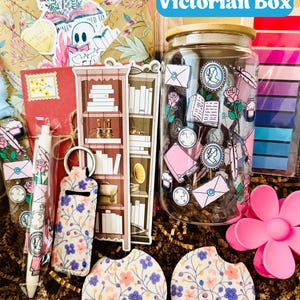 May include: A Victorian Box gift set with a variety of items. Includes a glass jar with a wooden lid, stickers, a pen, a keychain, coasters, and a decorative flower. The box contains a floral patterned envelope and other stationery items.