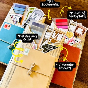 May include: A collection of stationery items, including bookmarks, sticky tabs, a greeting card, and bookish stickers. The items are bundled together with twine and presented on a wooden surface. The text "BOOK ONLY includes..." is visible.