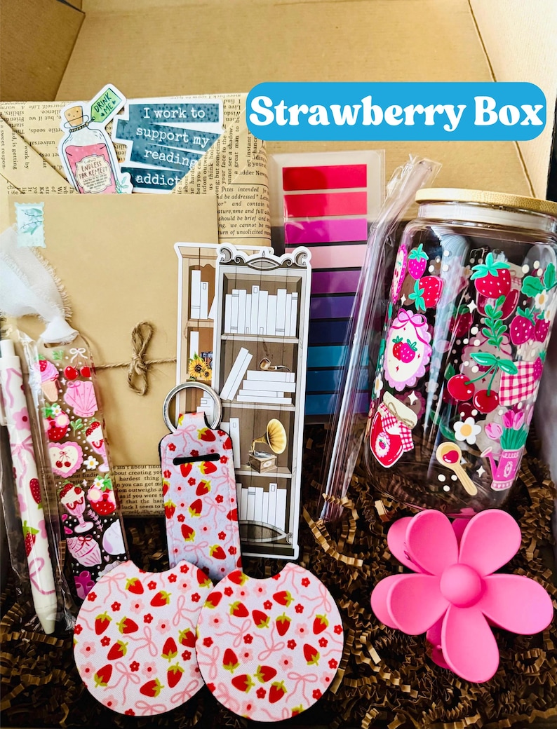 May include: A gift box labeled "Strawberry Box" filled with various items. Includes a decorated jar, pens, stickers, coasters, a keychain, and a flower-shaped phone holder. The items feature strawberry and floral designs.