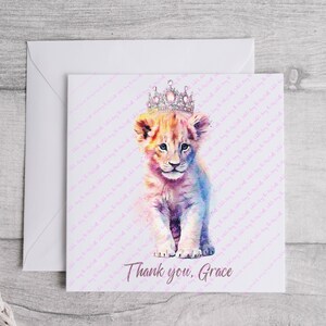 K&ouml;nnte beinhalten: Eine Aquarell-Illustration eines L&ouml;wenjungen mit einer glitzernden Krone. Der Junge ist hellbraun mit rosa und blauen Akzenten. Der Hintergrund ist wei&szlig; mit einem rosa Muster. Der Text "Danke, Grace" befindet sich am unteren Rand der Karte.