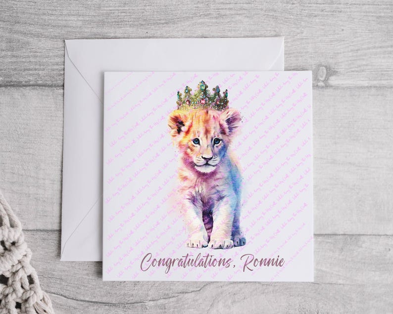 K&ouml;nnte beinhalten: Eine Aquarell-Illustration eines L&ouml;wenjungen mit einer glitzernden Krone. Der Junge ist hellrosa und wei&szlig; vor einem hellblauen Hintergrund. Der Text "Congratulations, Ronnie" ist unter dem Bild gedruckt.