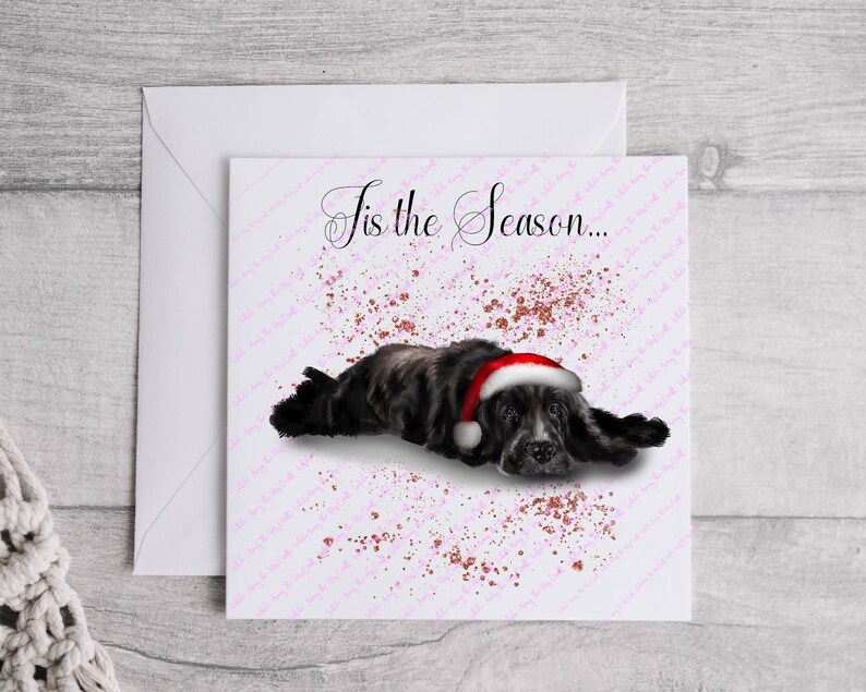 May include: A Christmas card featuring a black and gray dog wearing a red and white Santa hat. The card has the text "Tis the Season..." in elegant script, with a pink and brown speckled background.