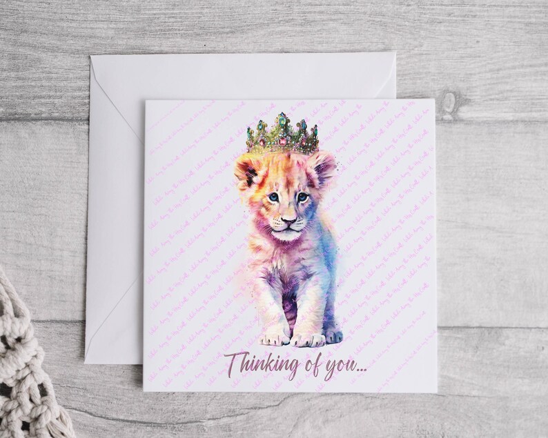 K&ouml;nnte beinhalten: Eine Aquarell-Illustration eines L&ouml;wenjungen mit einer glitzernden Krone. Das Junge steht auf einem wei&szlig;en Hintergrund mit einem rosa-wei&szlig;en Muster. Der Text "Thinking of you..." ist unter dem Jungen gedruckt.