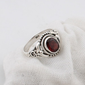 May include: A silver ring with a red gemstone set in a decorative bezel. The ring is marked "925" on the band.