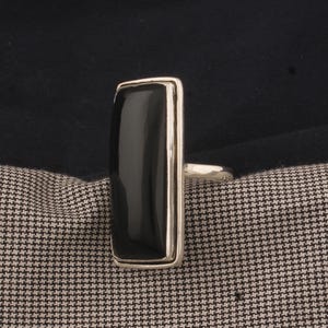 Könnte beinhalten: Ein silberner Ring mit einem schwarzen rechteckigen Stein.