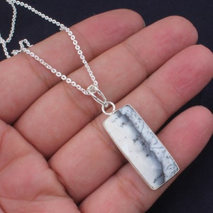 May include: A silver necklace with a rectangular pendant. The pendant has a white and grey patterned stone, set in a silver frame, suspended from a fine silver chain. The necklace is shown against a neutral backdrop.