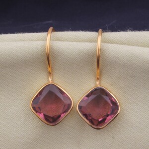 May include: A pair of gold dangle earrings with square-shaped, faceted, purple gemstones.