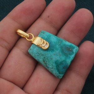 May include: A turquoise green gemstone pendant with a gold bail and a gold setting. The pendant is in the shape of a rectangle with rounded corners.