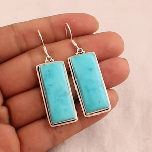 May include: A pair of silver dangle earrings featuring rectangular turquoise stones. The stones are a light blue colour and have a smooth, polished finish.