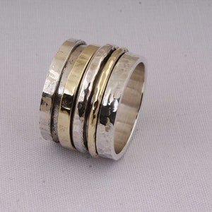 Könnte beinhalten: Ein drehbarer Silber- und Goldring mit gehämmerter Textur. Der Ring besteht aus mehreren Bändern, die sich frei drehen.
