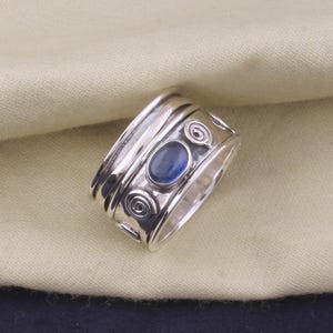 May include: A silver ring with a blue gemstone and a swirling design.