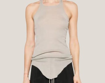 Könnte beinhalten: Ein hellbeigefarbenes Haltertop mit rundem Ausschnitt und einem einzigartigen asymmetrischen Saum. Das Top ist aus einem weichen, gerippten Material gefertigt. Das Model trägt eine schwarze Hose.