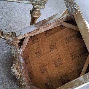 May include: The underside of a chair seat with a woven fabric seat. The chair is made of wood and has a distressed white paint finish with gold accents.