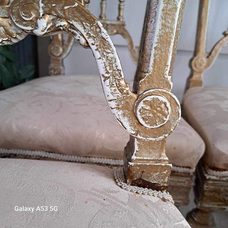 May include: Two antique chairs with white and gold painted wooden frames. The chairs have ornate carvings and are upholstered in a cream-colored fabric.