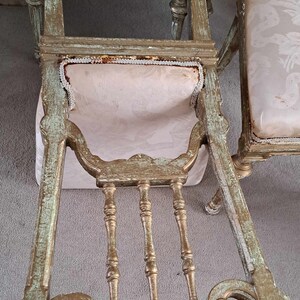 May include: A pair of antique chairs with ornate carvings and a distressed gold finish. The chairs have a light pink fabric upholstery with a white trim.