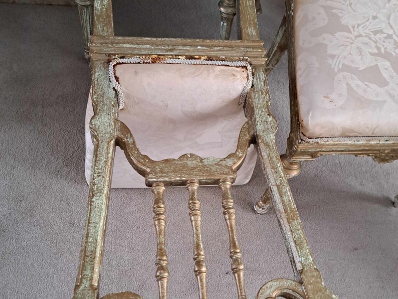 May include: A pair of antique chairs with ornate carvings and a distressed gold finish. The chairs have a light pink fabric upholstery with a white trim.