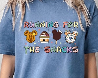 May include: A blue t-shirt with the text "Running for the Snacks" in rainbow colors. The text is surrounded by four cartoon Mickey Mouse heads, each holding a different snack: a waffle, ice cream, a Mickey Mouse-shaped ice cream bar, and a donut.
