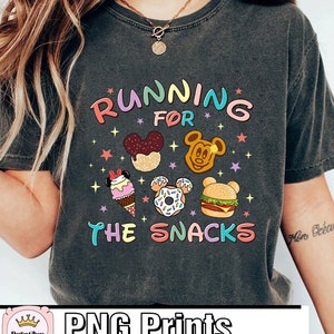May include: A gray t-shirt with the text "Running for the Snacks" in rainbow colors. The design includes cartoon images of Mickey Mouse ears, ice cream cones, donuts, and hamburgers.