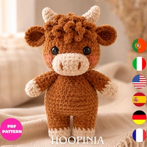 Peut inclure: Une peluche au crochet marron et crème en forme de vache highland avec des cheveux bouclés, deux petites cornes, des yeux noirs et des joues roses. Le jouet a une finition en fil texturé et se tient debout. Un cercle rose indique PDF PATTERN.