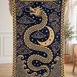 May include: A rectangular crochet blanket featuring a dark blue background with a gold dragon, crescent moon, stars, and stylized clouds. The border consists of a repeating geometric diamond pattern in gold and dark blue, with wave motifs at the bottom.