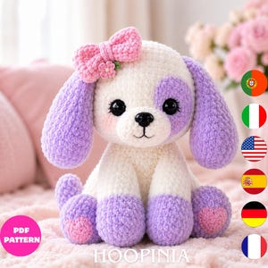 Peut inclure: Un jouet en peluche crocheté représentant un chien au corps blanc avec des oreilles, des pattes et une tache sur l'œil de couleur lavande. Il porte un nœud rose avec une petite fleur, des yeux noirs, un nez noir et des coussinets en forme de cœur.
