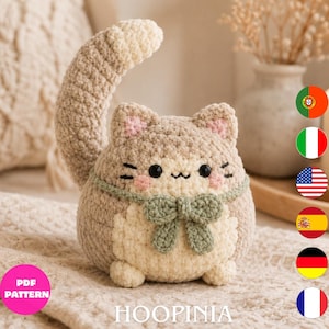 Peut inclure: Un jouet en peluche chat crocheté et rond avec un corps beige et crème, une longue queue courbée et un nœud vert sauge autour du cou. Le chat a des yeux brodés noirs, une petite bouche et des joues roses. Le texte PDF PATTERN HOOPINIA est visible.