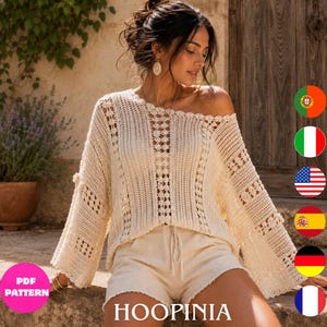 May include: An off-white, long-sleeved crochet jumper featuring an open-knit pattern with vertical panels and a scalloped neckline, paired with matching off-white shorts. The garment has a loose, relaxed fit with wide sleeves and a textured design.