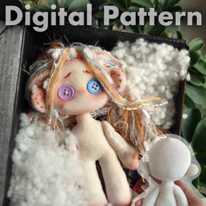Könnte beinhalten: Eine handgefertigte Puppe mit Knopfaugen und bunten Garnhaaren, präsentiert in einer Box mit Füllung. Die Puppe hat einen hellen Hautton und rosige Wangen. Der Text "Digital Pattern" befindet sich oben im Bild.
