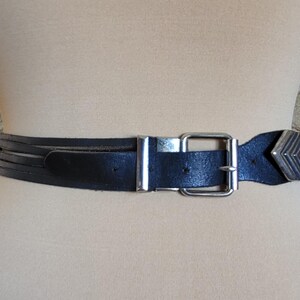 May include: Black leather belt with a silver-tone buckle and a decorative arrow-shaped end. The belt has multiple thin straps and a classic, adjustable design. A stylish accessory for various outfits.
