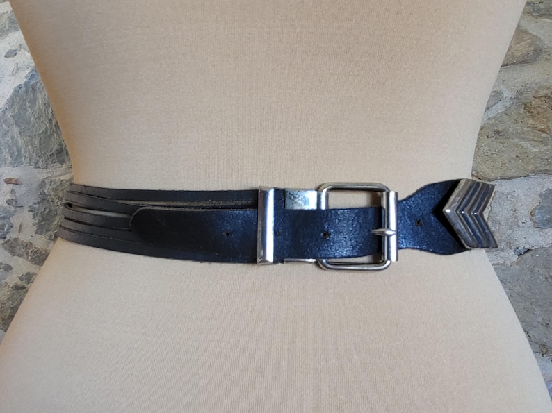 May include: Black leather belt with a silver-tone buckle and a decorative arrow-shaped end. The belt has multiple thin straps and a classic, adjustable design. A stylish accessory for various outfits.