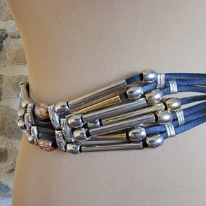 May include: A wide belt with multiple navy blue leather straps and silver-toned metal accents. The belt features decorative silver tubes and rounded silver clasps, creating a bold, stylish accessory.