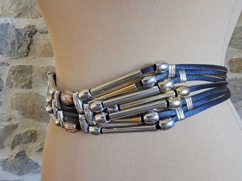 May include: A wide belt with multiple navy blue leather straps and silver-toned metal accents. The belt features decorative silver tubes and rounded silver clasps, creating a bold, stylish accessory.