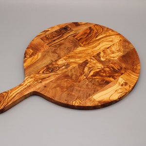May include: A round olive wood cutting board with a handle. The board has a natural wood grain pattern and is perfect for serving cheese, charcuterie, or other appetizers.