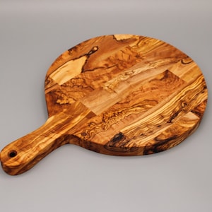 May include: A round olive wood cutting board with a handle. The board has a natural wood grain pattern and is perfect for serving cheese, charcuterie, or other appetizers.