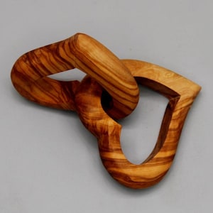 May include: A wooden sculpture of two intertwined hearts, carved from olive wood. The hearts are connected in a way that suggests a strong bond or connection.