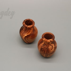 May include: Two small, wooden vases with a natural wood grain pattern. The vases are made of olive wood and have a rustic, handcrafted look.