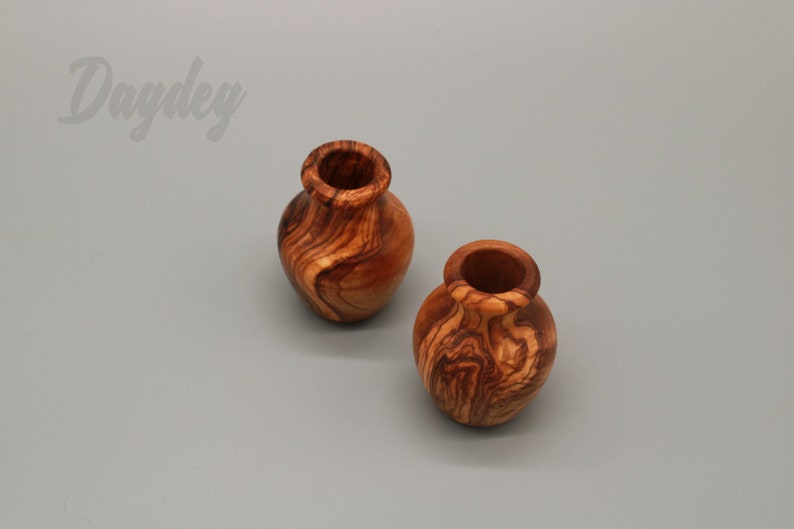 May include: Two small, wooden vases with a natural wood grain pattern. The vases are made of olive wood and have a rustic, handcrafted look.
