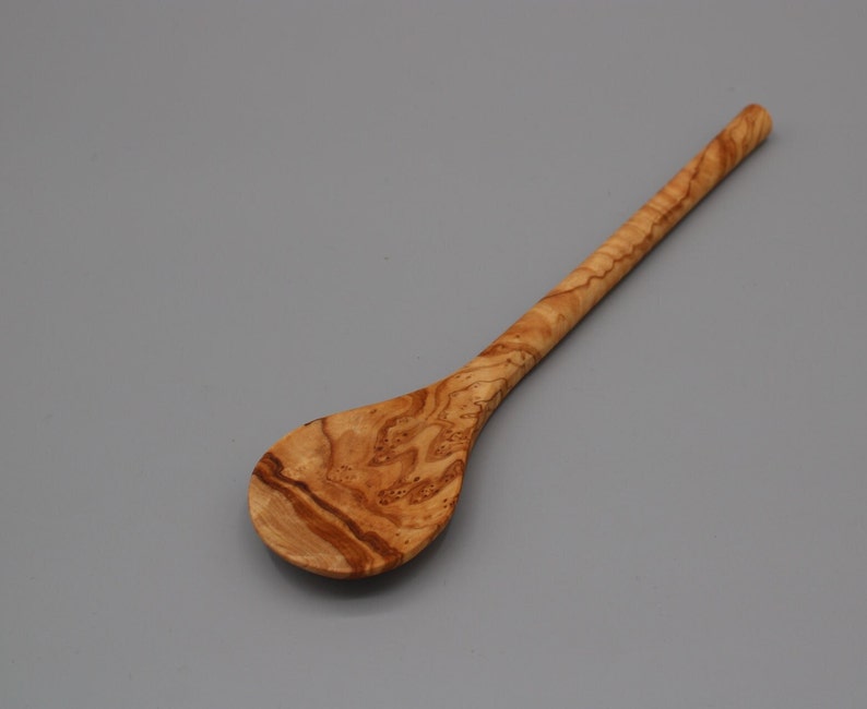 Op de afbeelding: Een houten lepel met een natuurlijk houtnerfpatroon. De lepel heeft een lange steel en een ronde kom.