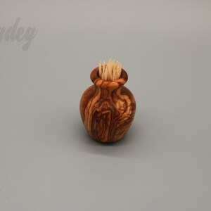 May include: A small wooden olive wood toothpick holder in the shape of a vase with toothpicks inside.