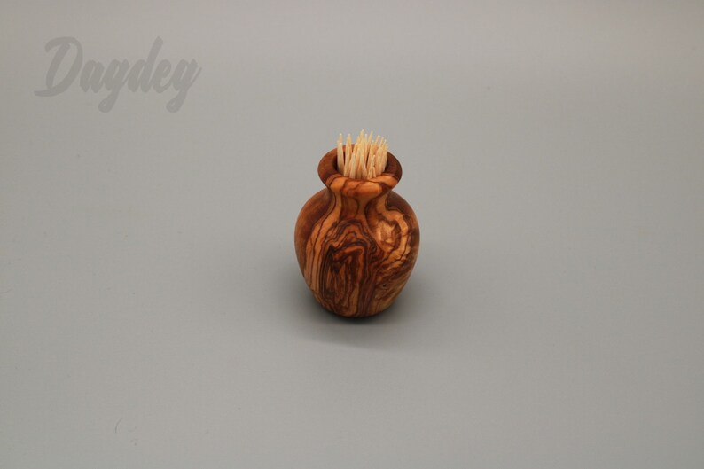 May include: A small wooden olive wood toothpick holder in the shape of a vase with toothpicks inside.