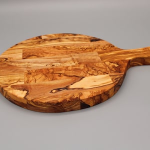 May include: A round olive wood cutting board with a handle. The board has a natural wood grain pattern and is perfect for serving cheese, bread, or other appetizers.