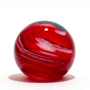 May include: A vibrant red glass sphere with swirling patterns and iridescent accents. The decorative orb has a smooth, polished surface and a slight shadow, set against a white background. The sphere is a decorative art object.
