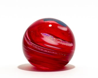 May include: A vibrant red glass sphere with swirling patterns and iridescent accents. The decorative orb has a smooth, polished surface and a slight shadow, set against a white background. The sphere is a decorative art object.