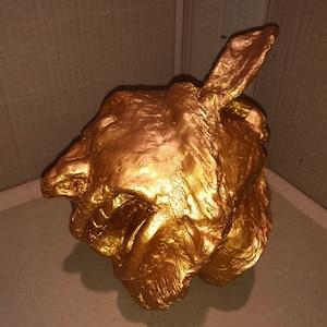 May include: A gold-colored, abstract sculpture of a face with a textured surface.