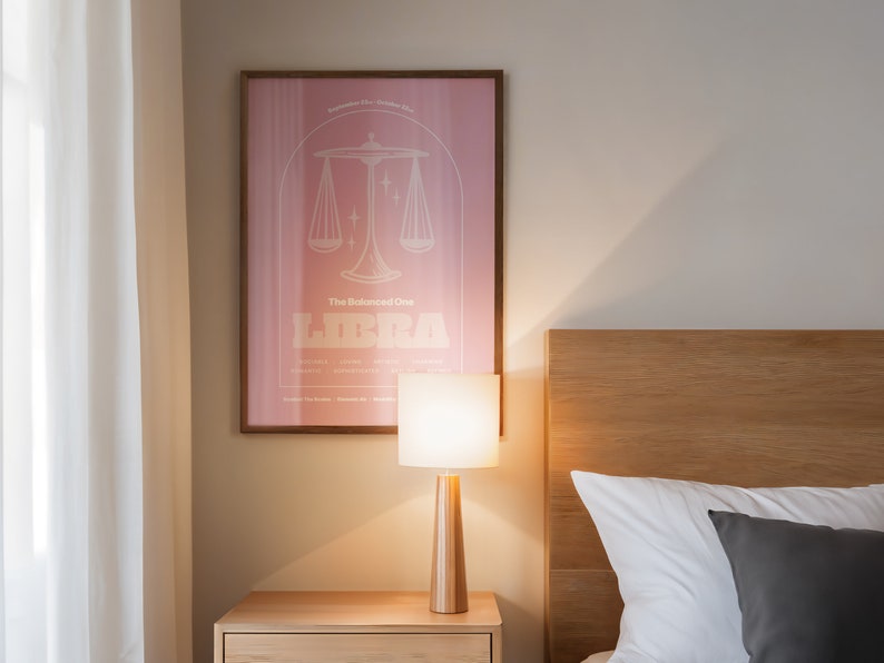 Może przedstawiać: R&oacute;żowo-biały plakat z ilustracją znaku zodiaku Wagi i tekstem "The Balanced One Libra". Plakat jest oprawiony i wisi na białej ścianie nad drewnianym zagł&oacute;wkiem z białą i szarą poduszką.