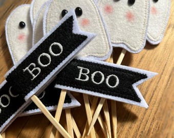 May include: Set of six white felt ghost cupcake toppers with black felt eyes and pink cheeks. Each ghost has a black felt banner with white embroidery that reads "BOO".