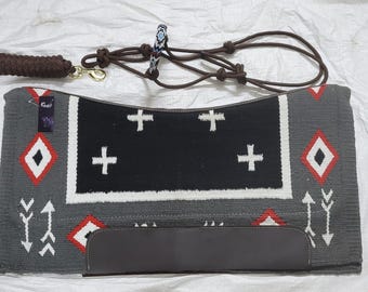 May include: A gray and black saddle pad with a white and red geometric pattern. The pad has a black leather flap with a white border. The pad is designed for use with a horse saddle.