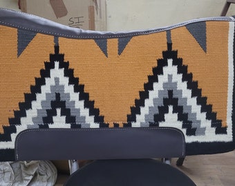 May include: A saddle pad with a geometric pattern in shades of black, white, gray, and orange. The pad has a black leather border.