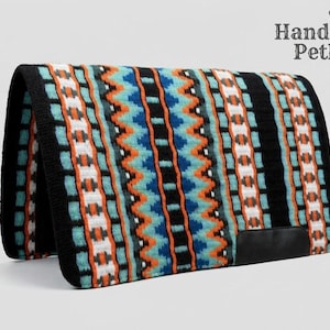 Op de afbeelding: Een kleurrijk zadeldek met een zwarte rand en een geometrisch patroon in turquoise, oranje en wit. Het dek heeft een zwart leren patch in de rechter benedenhoek. Het Handmade Pethub-logo staat in de rechterbovenhoek.