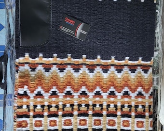 Op de afbeelding: Zwart zadeldek met een geometrisch patroon in bruin, wit en zwart. Het heeft een zwart leren patch en een visitekaartje met de tekst "Cavalry International".
